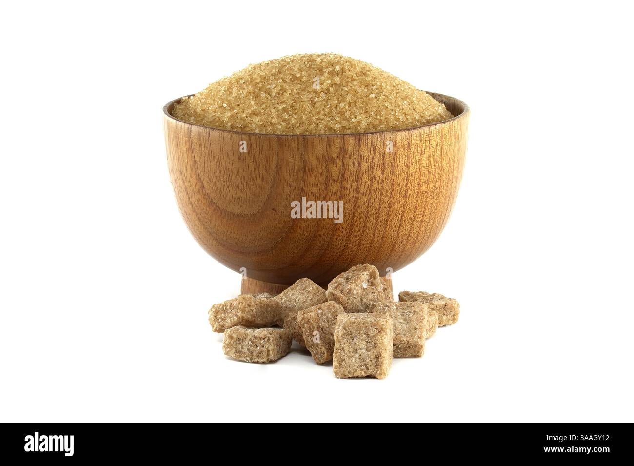 A wooden bowl is filled with granulated brown sugar, with sugar cubes scattered below, set against a clean white background. Stock Photo