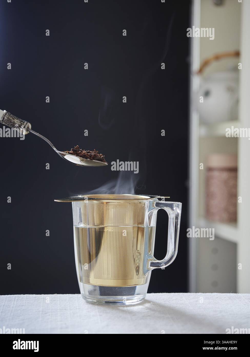 Spoon with roibois red tea on glass cup with steaming hot water with golden metallic filter Stock Photo