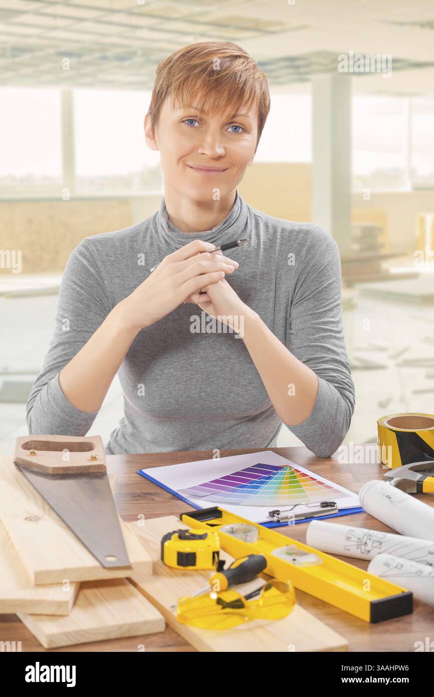 Female construction worker sitting at table with tools Stock Photo