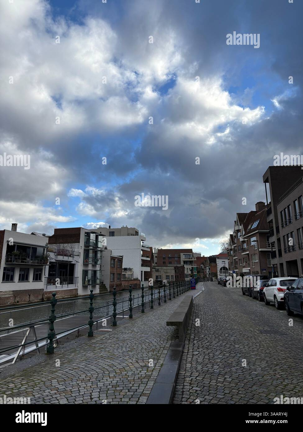 Cobblestone pathway along a serene canal, lined with historic European buildings under a dramatic, cloudy sky. - Smartphone Captured Stock Image