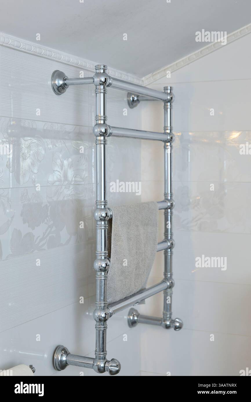 Chrome towel rack fixed to a bathroom wall with white floral tiles ...