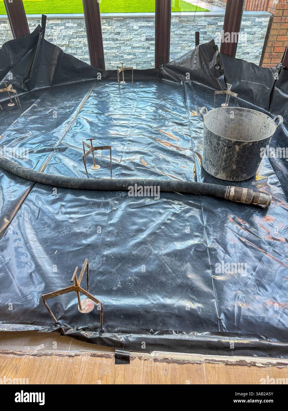 Plastic membrane , levelling equipment and hose on the floor of a new conservatory ready for concrete screed to be pumped into the area. No people. - Smartphone Captured Stock Image