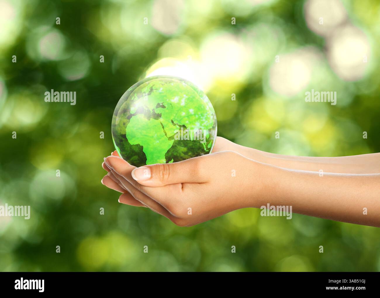 Woman holding glass ball with Earth globe inside on blurred green background, closeup. Concept of environment protection Stock Photo