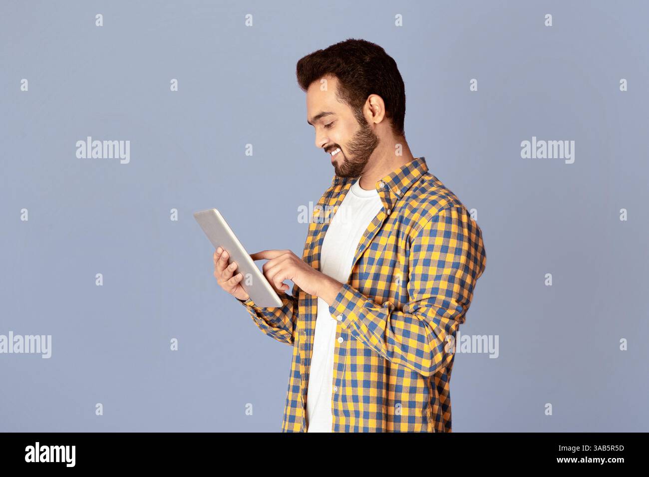 Handsome Indian guy using tablet computer for online work or communication on violet background Stock Photo