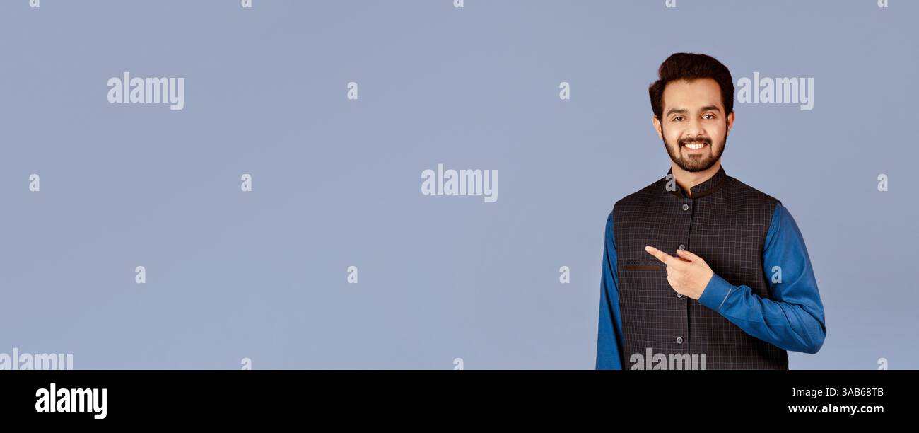 Handsome young Indian man smiling and pointing aside over lilac background Stock Photo