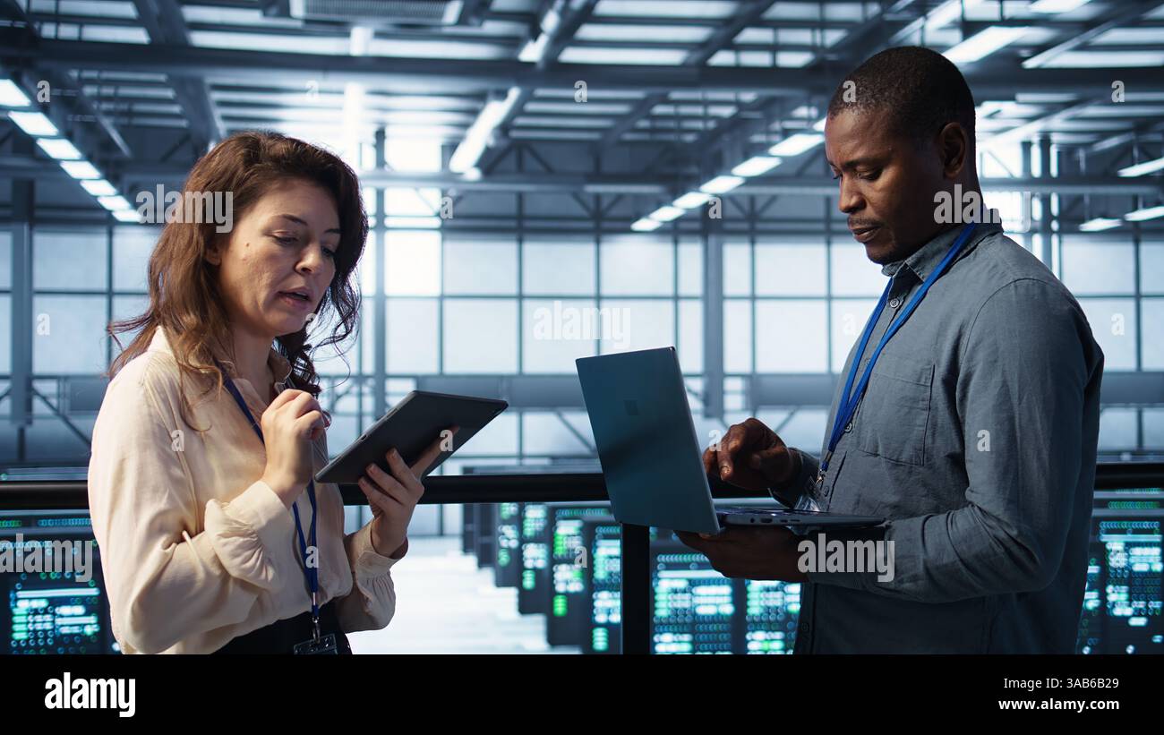 System administrators using notebook device in data center, managing server virtualization. IT specialists using laptop in server farm, sustaining long term infrastructure reliability, camera B Stock Photo