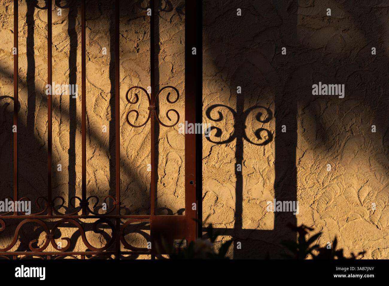 Ornamental gate casting shadows on textured wall Stock Photo