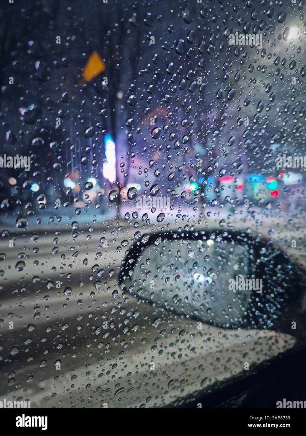 Melting snow water drops on the car window with view to the outside mirror. Winter night urban scene - Smartphone Captured Stock Image