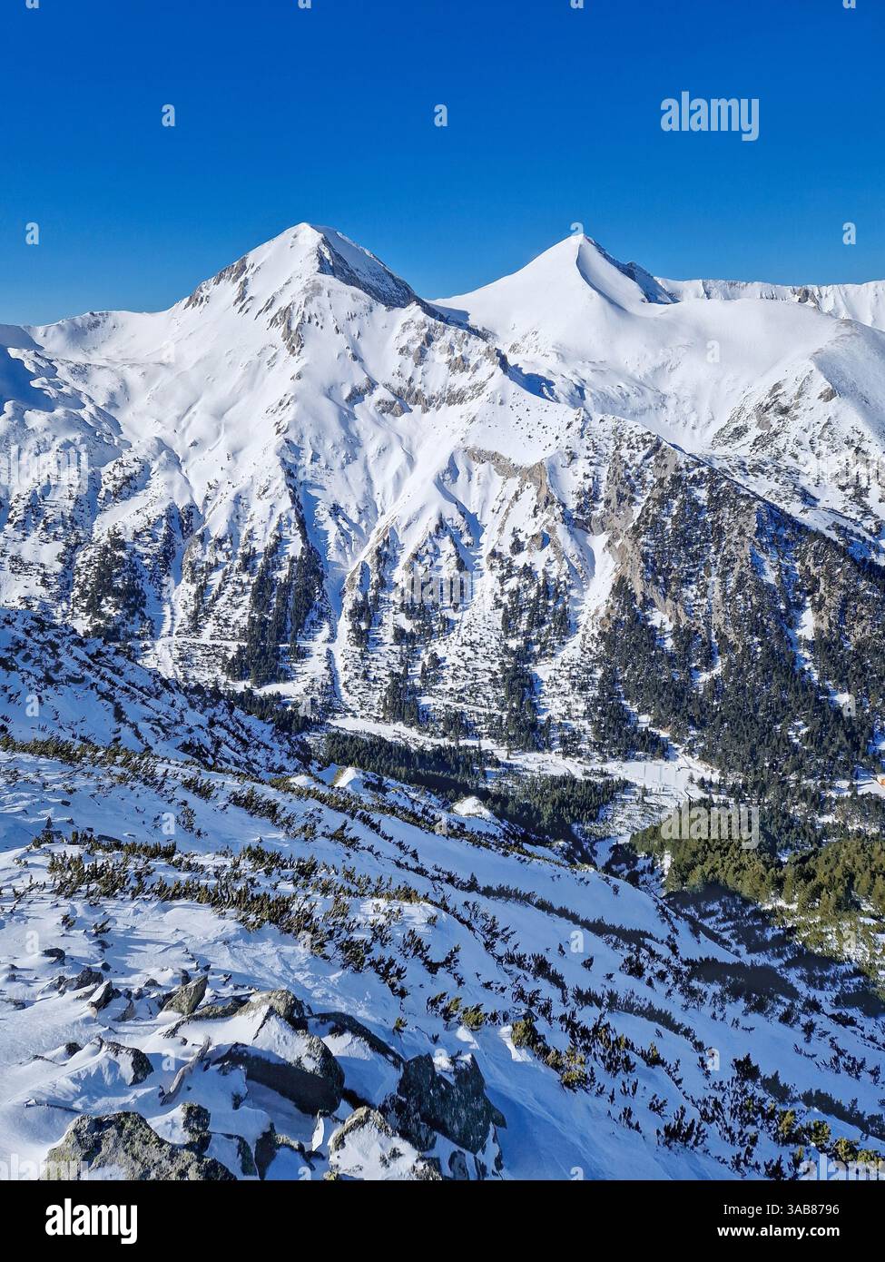 Aerial view above the Pirin mountains with rocky peaks covered with snow. Winter view at Bansko ski resort in Bulgaria - Smartphone Captured Stock Image