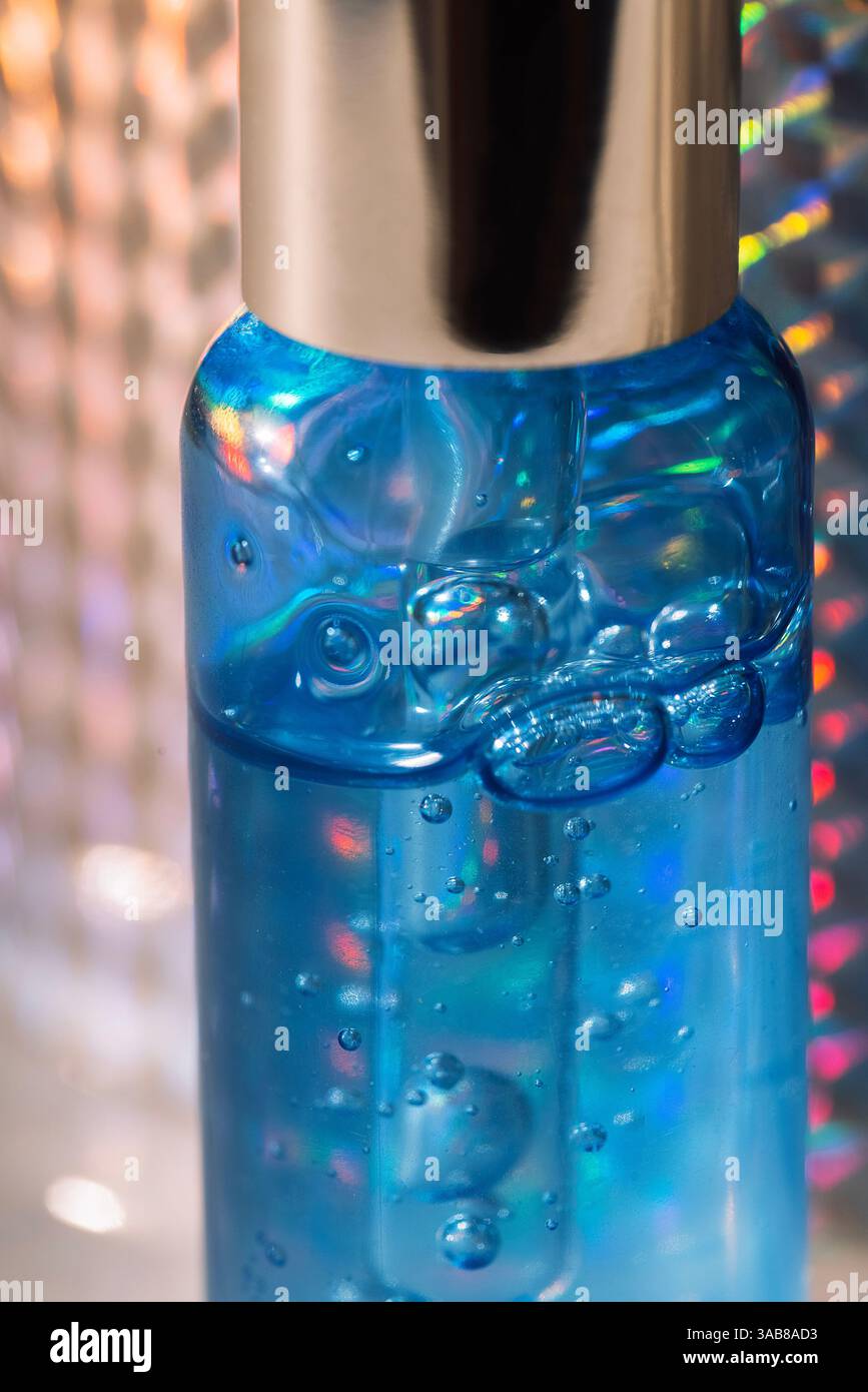 Close-up of a blue bottle of moisturizing serum with bubbles and a pipette. Cosmetic products. Vitamin essence with a dropper on a holographic silver Stock Photo