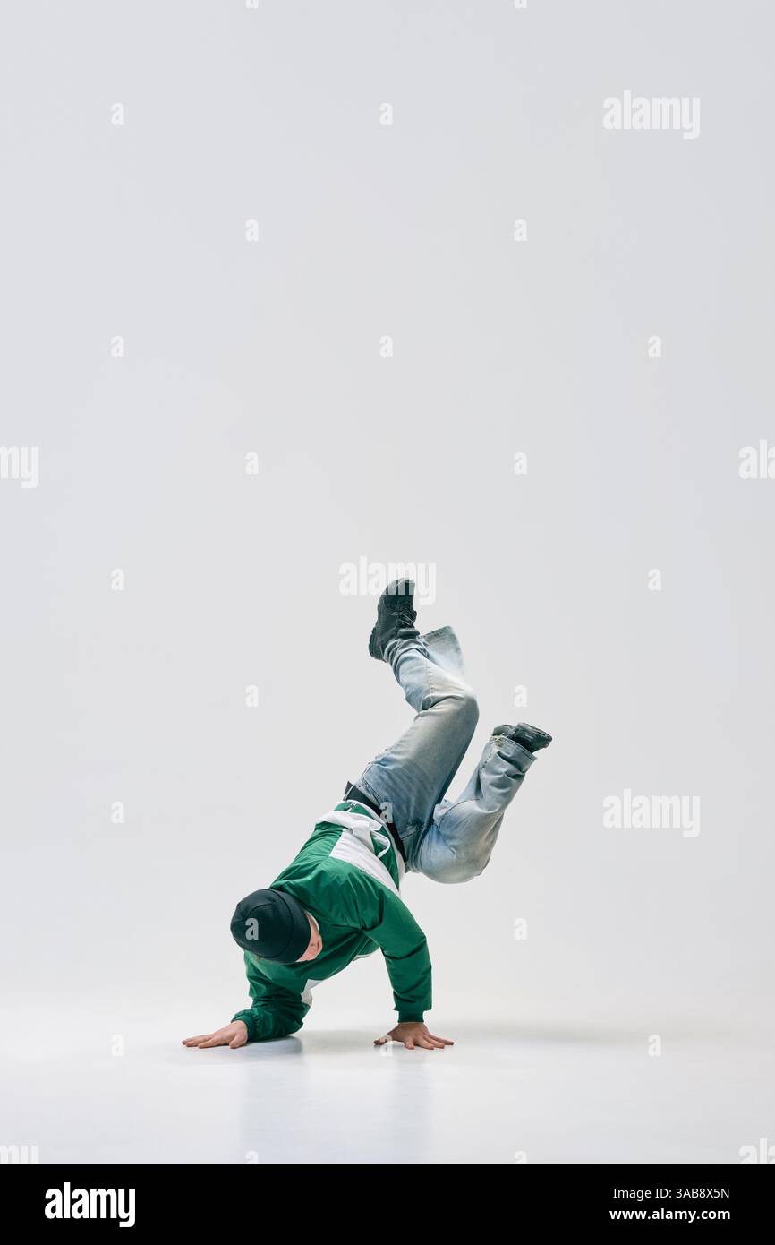 Breakdancer twisting mid-air while balancing on hands, showcasing flexibility and agility against white studio background. Stock Photo