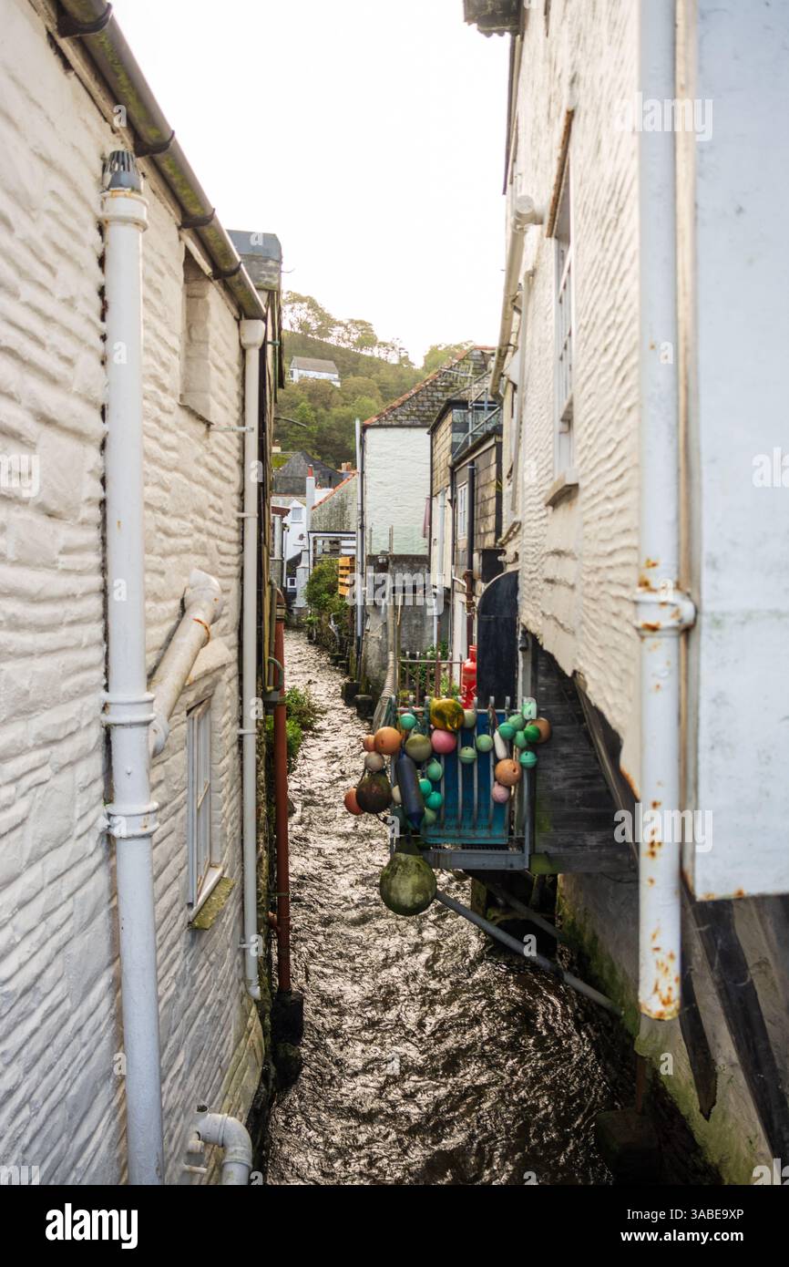 A narrow waterway flows between buildings in Polperro, adorned with colorful buoys. A unique feature of this Cornish village. Stock Photo