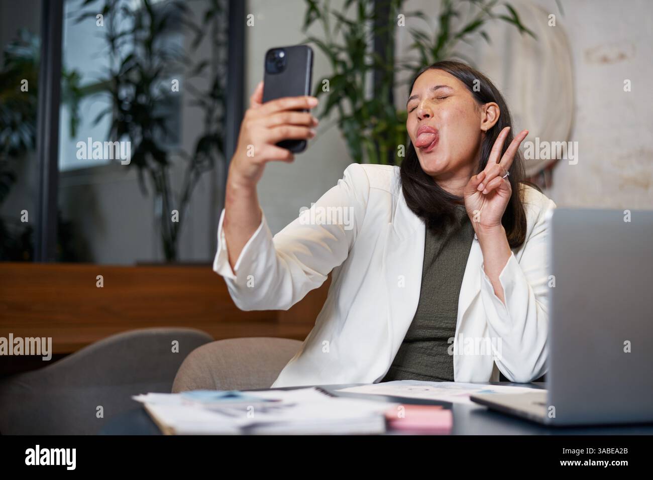 Professional Woman Taking a Fun Selfie While Sitting in a Modern Office Workspace Stock Photo