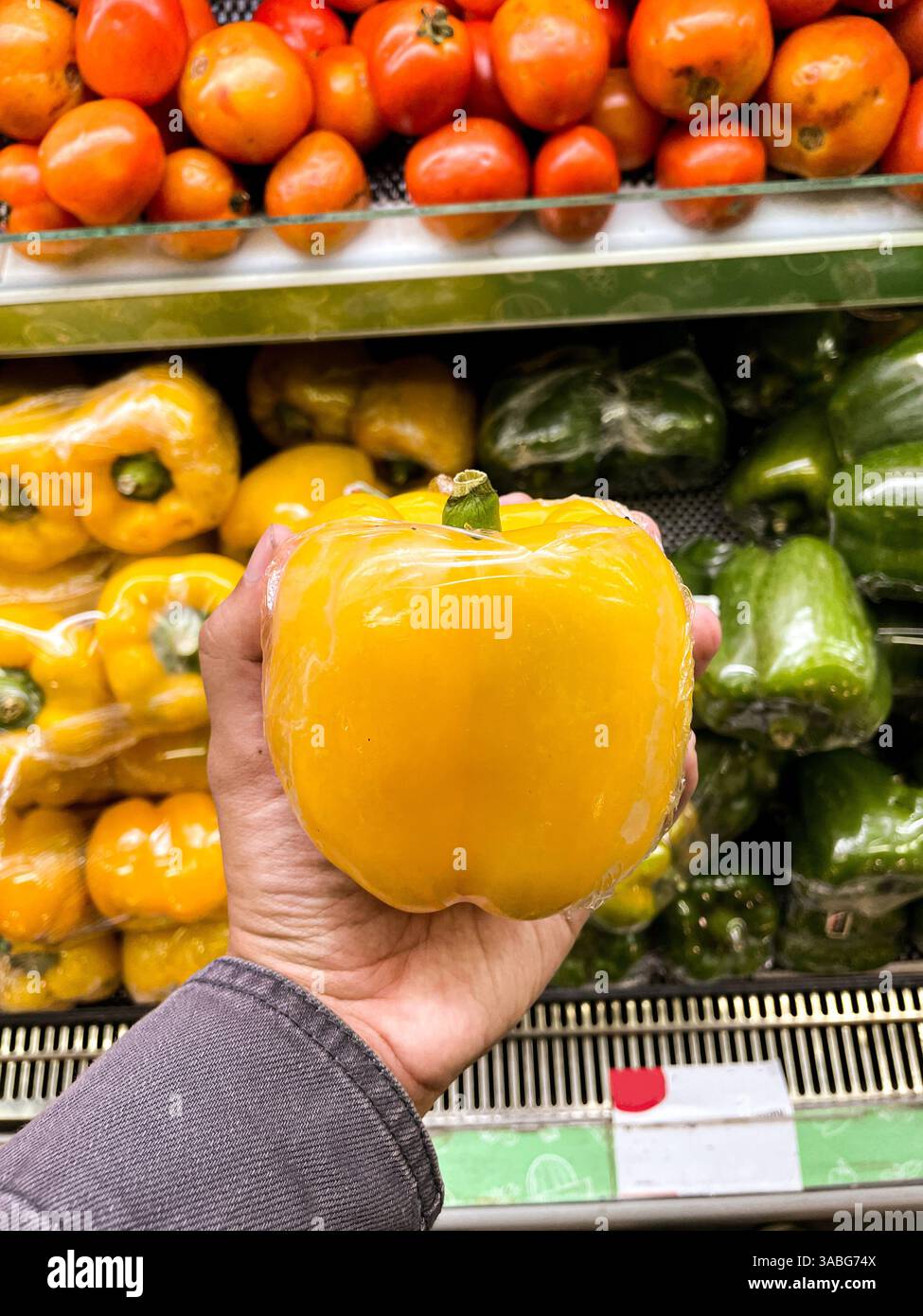 hand holding yellow bell pepper or paprika on groceries market - Smartphone Captured Stock Image