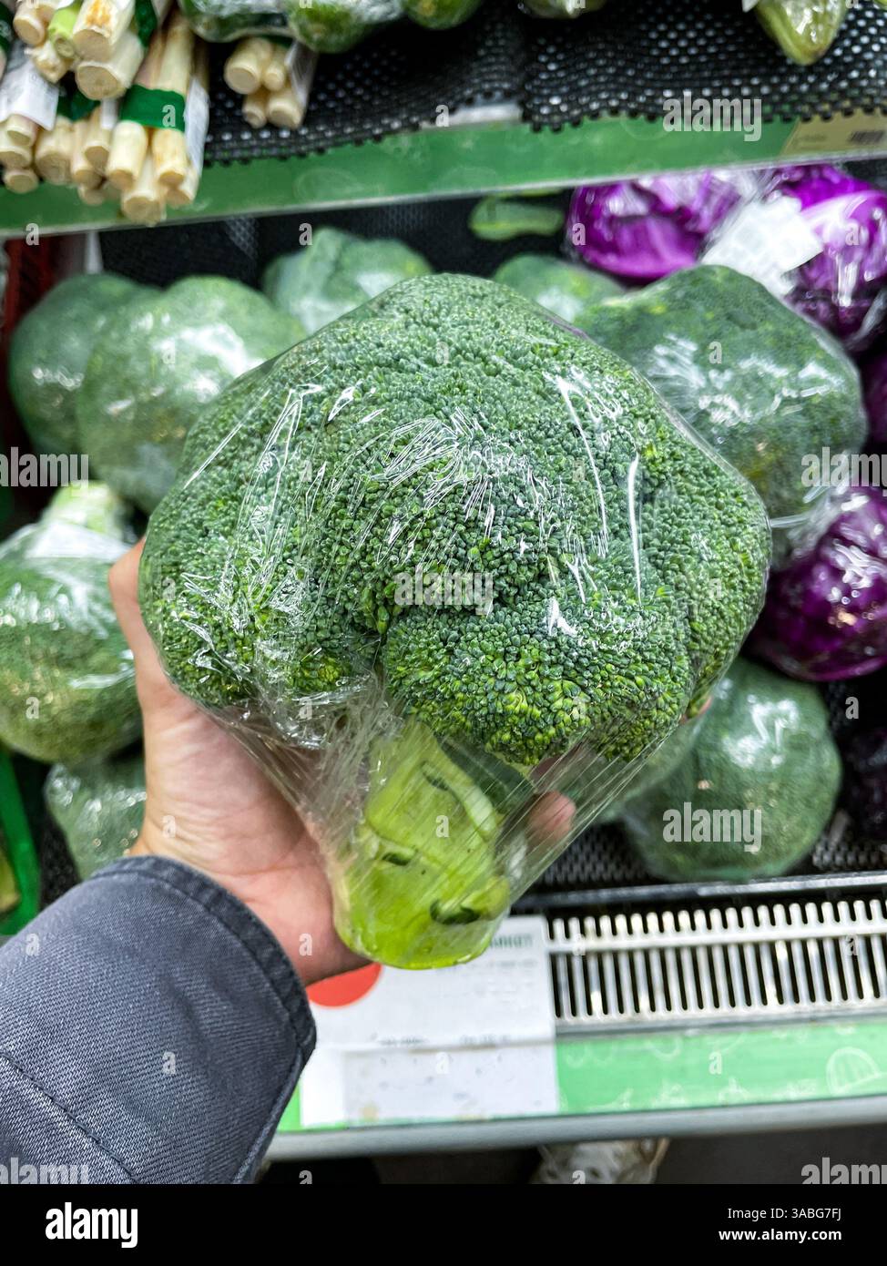 hand holding fresh broccoli wrapped in plastic at groceries store - Smartphone Captured Stock Image