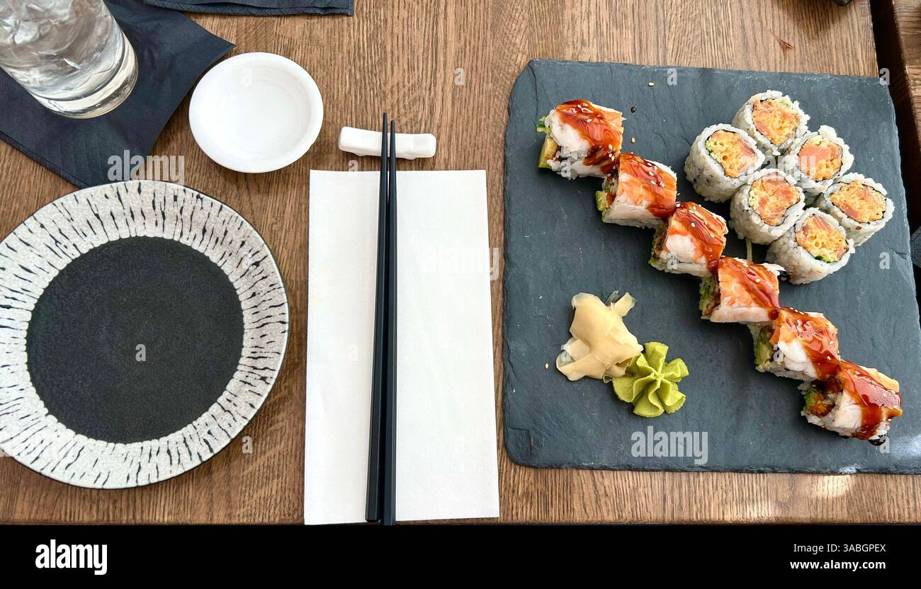 Elegant sushi rolls served on a textured rock plate, accompanied by chopsticks and a soy sauce bowl. - Smartphone Captured Stock Image