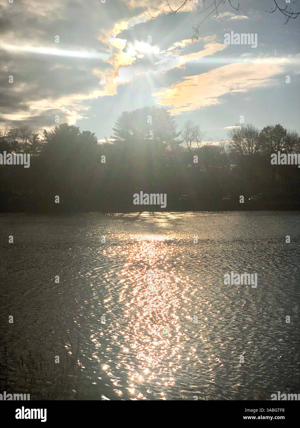 A stunning view of the sun peeking through soft, billowy clouds over a tranquil lake. - Smartphone Captured Stock Image
