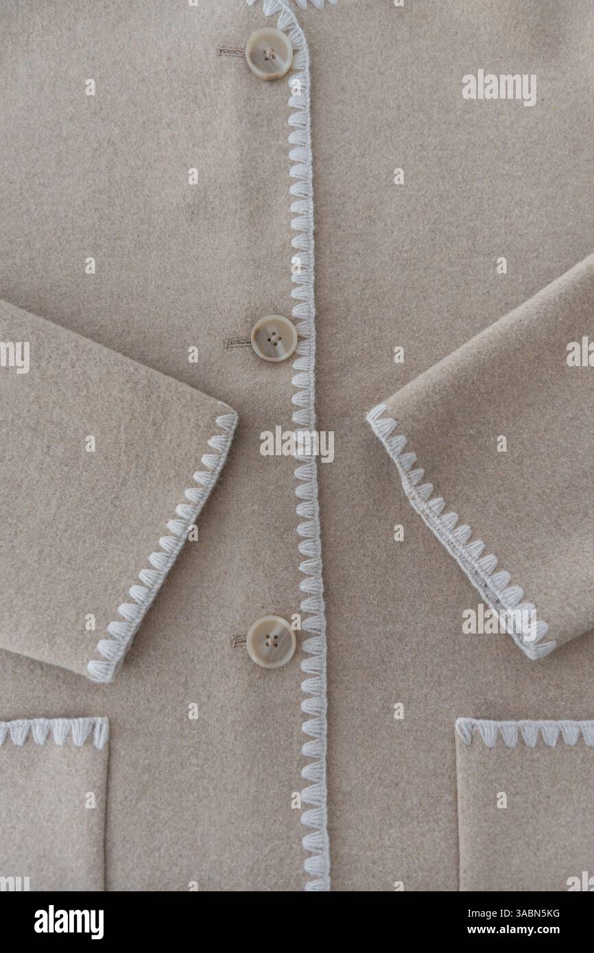 Beige wool blend coat with white embroidered trim and buttons, close-up view Stock Photo