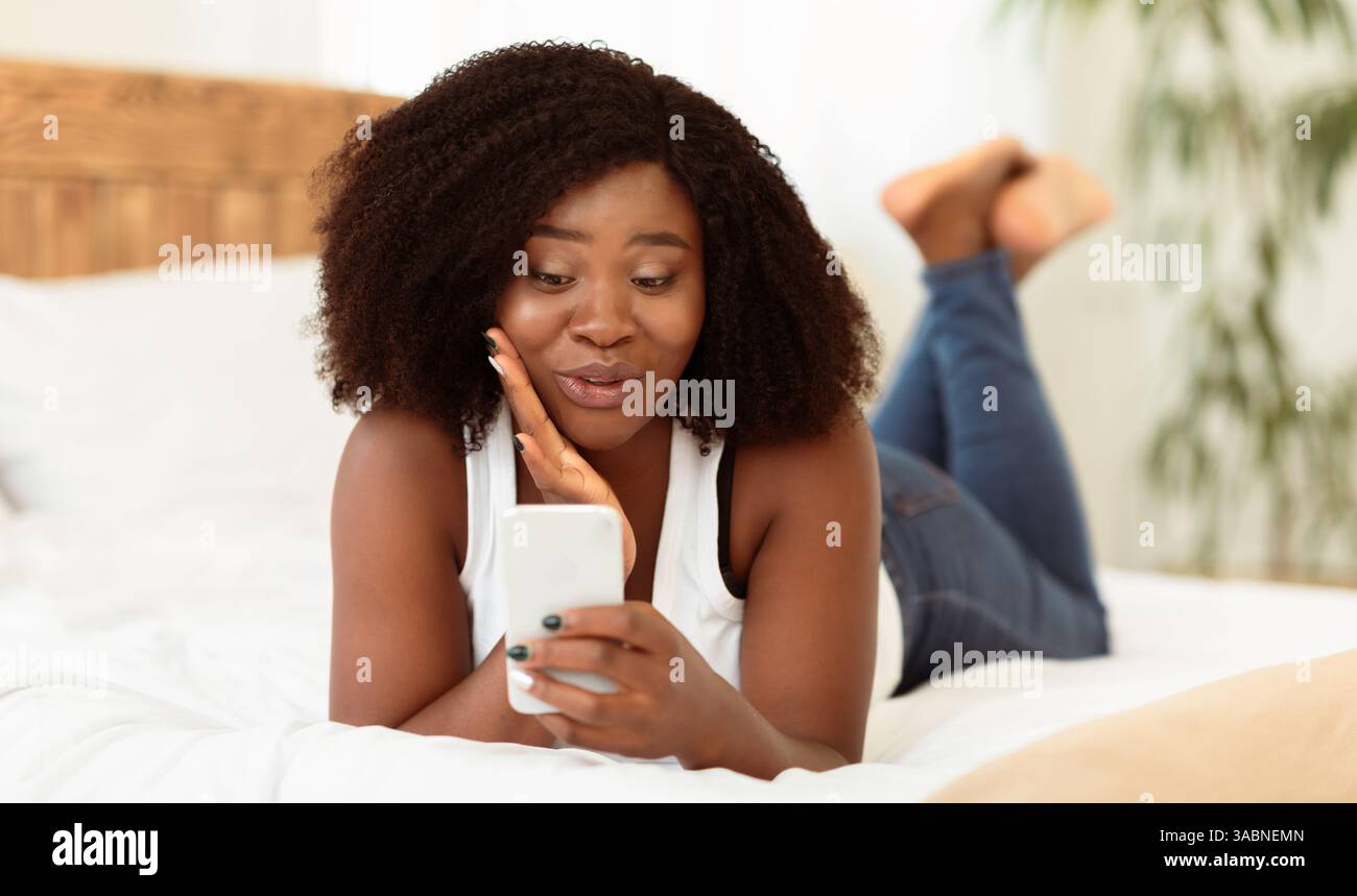 Cute black girl lying on bed, using cell phone Stock Photo - Alamy