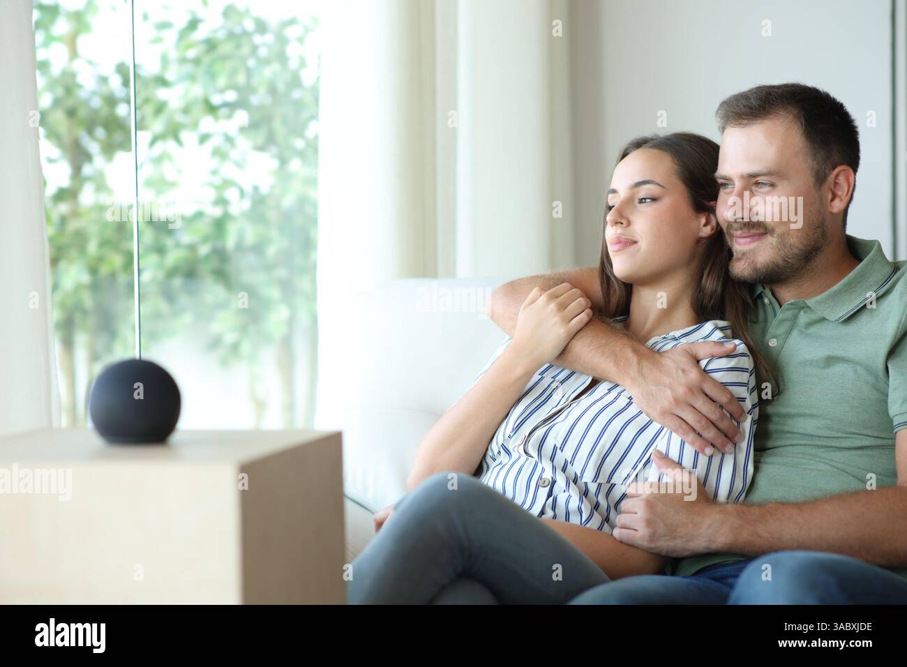 Couple relaxing sitting on a sofa at home with smart speaker Stock Photo