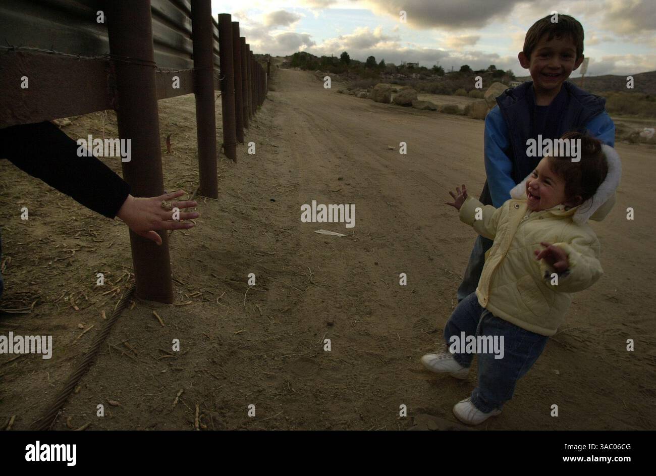 (PUBLISHED 03/03/2003, A-1): Not realizing the possibly disasterous implications, Jessica Mercado, 1, and brother Fernando Mercado Jr., 4, crawl under the US-Mexico border fence just out of reach of their mother, Norma Mercado, left. The US Border Patrol perched atop the hill at the end of the road, came swooping down just after someone handed the children back to their mother. The Mercados, like many other residents of Jacume, just south of the border, used to cross regularly without problems, to the neighboring town of Jacumba, to  buy groceries, use their post office box or visit friends an Stock Photo
