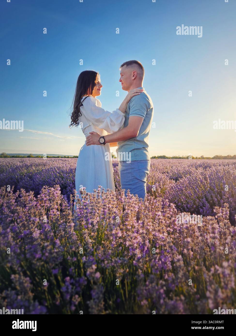 Young couple hugging together on a date in the lavender field. Picturesque summer scene, love and romance concept - Smartphone Captured Stock Image