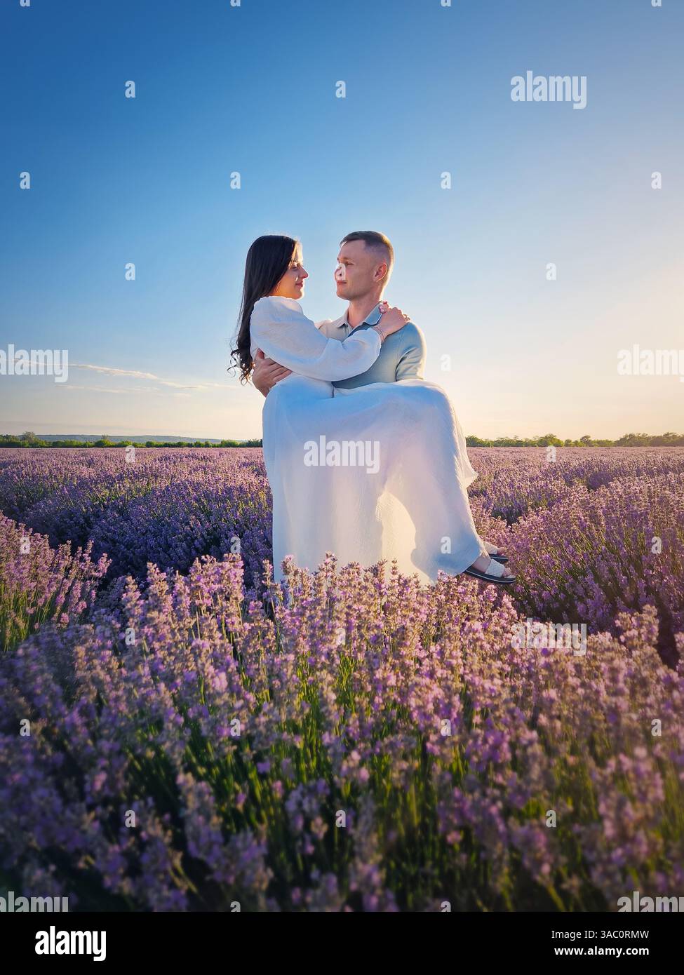 Young couple hugging together on a date in the lavender field. Picturesque summer scene, marriage love and romance concept - Smartphone Captured Stock Image
