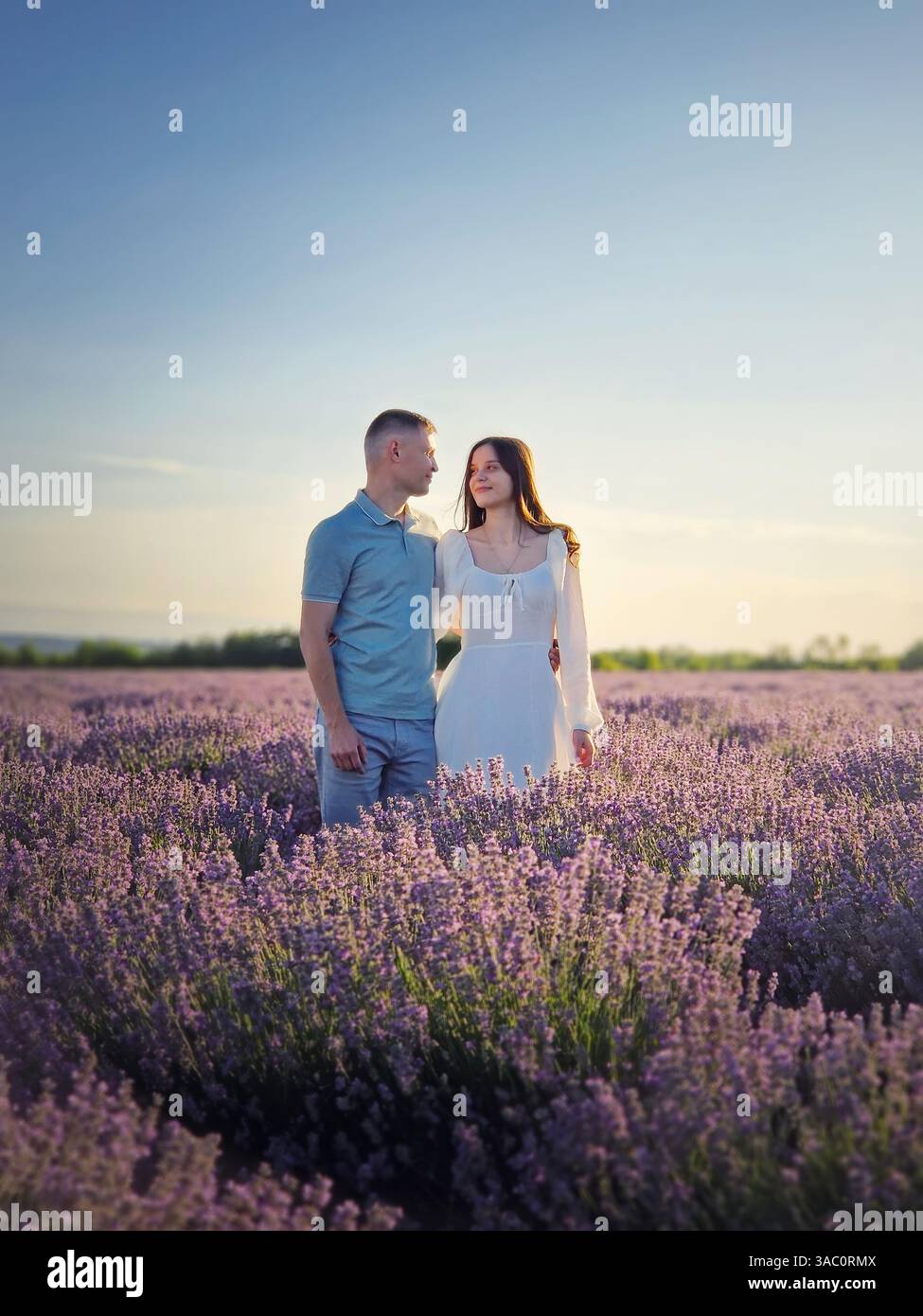 Young couple walking together on a date in the lavender field. Picturesque summer scenery. Love and romance marriage conceptual portrait - Smartphone Captured Stock Image