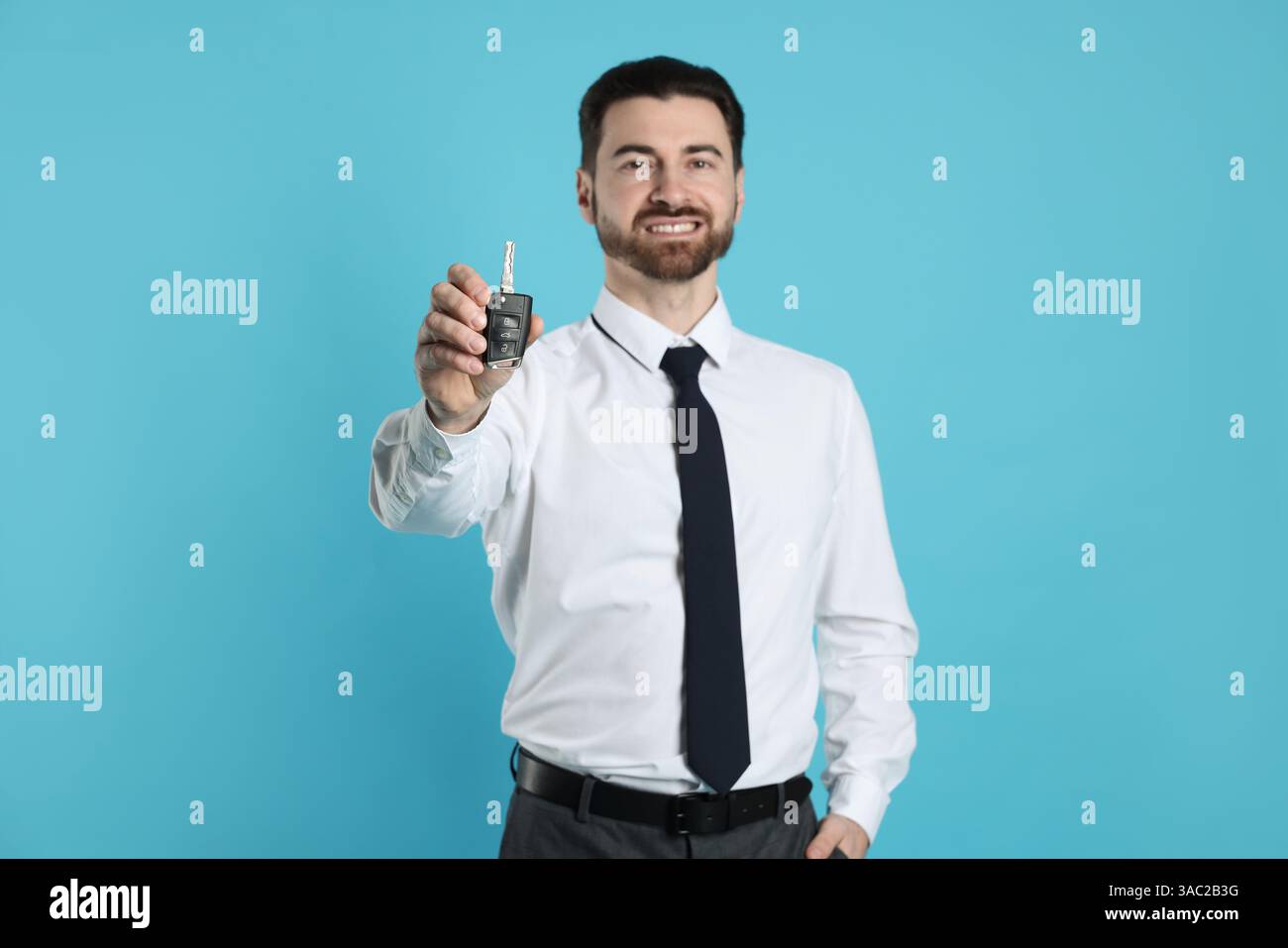 Cheerful salesman with car key on light blue background Stock Photo - Alamy