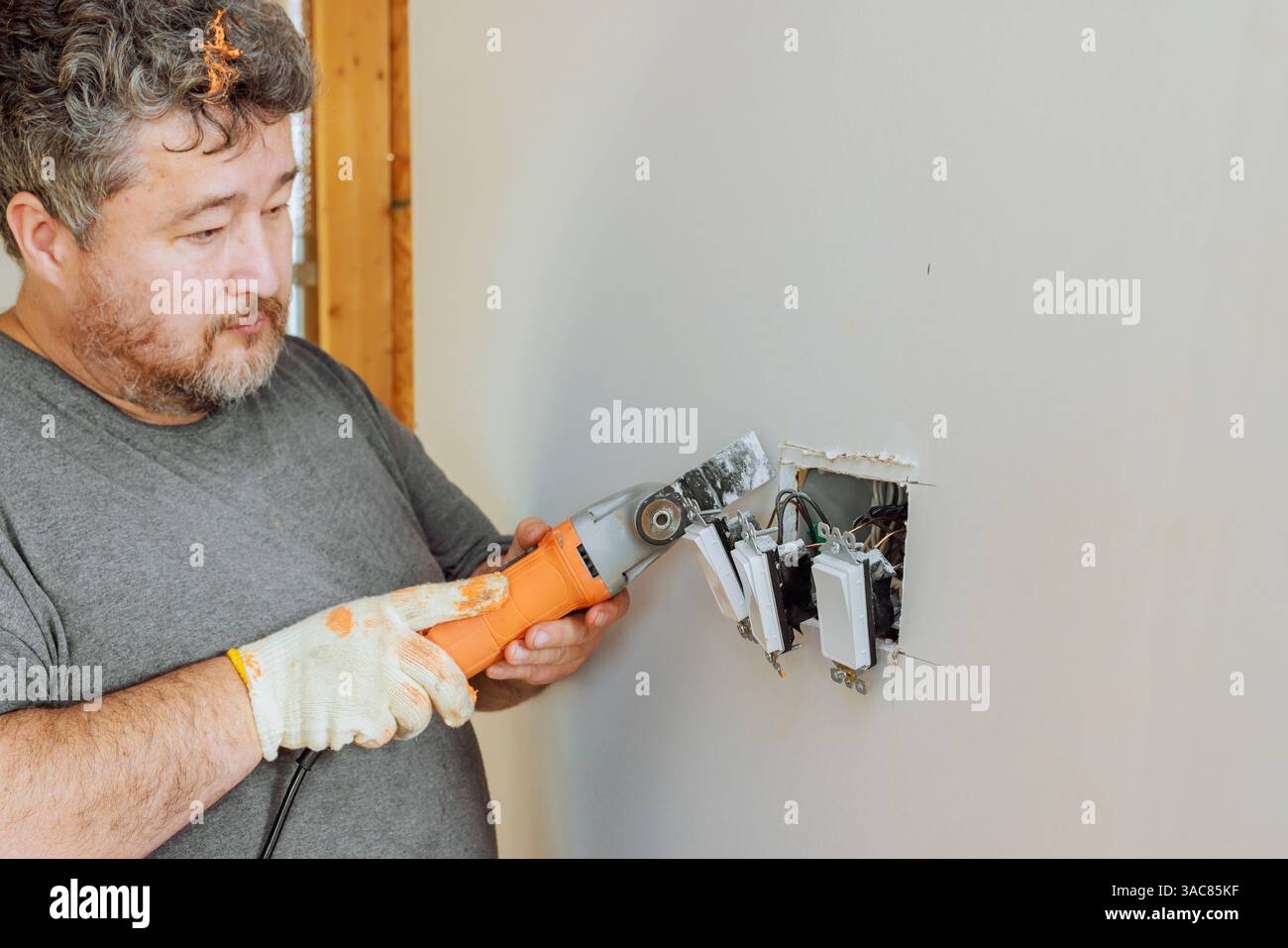 Electrician is using multi tool to work on electrical wiring in wall ...