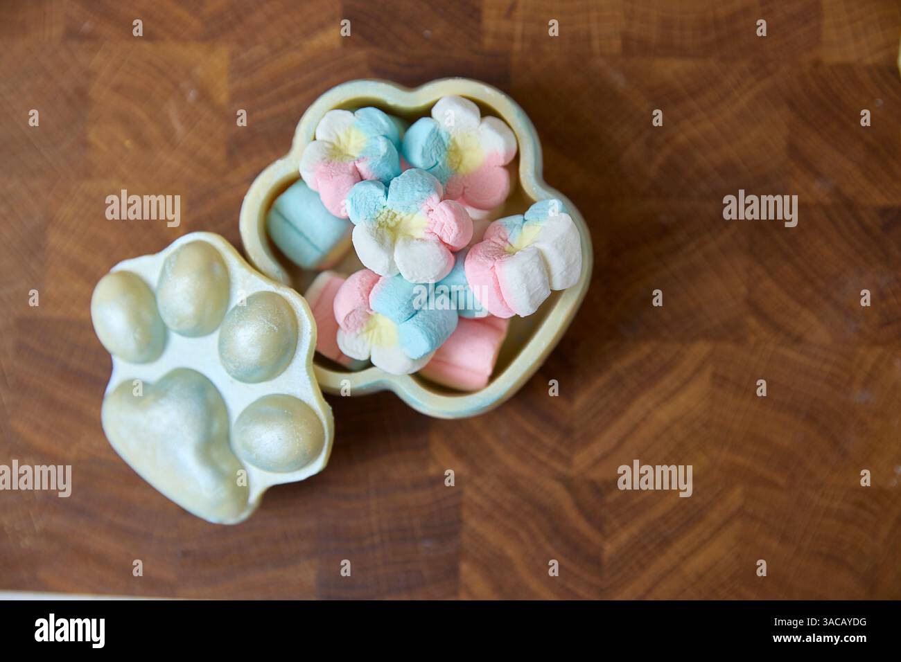 Radiant, pastel marshmallow candies gently burst from an opened, paw-shaped teal-toned tin, suggesting sweetness, comfort, and playful childhood memor Stock Photo