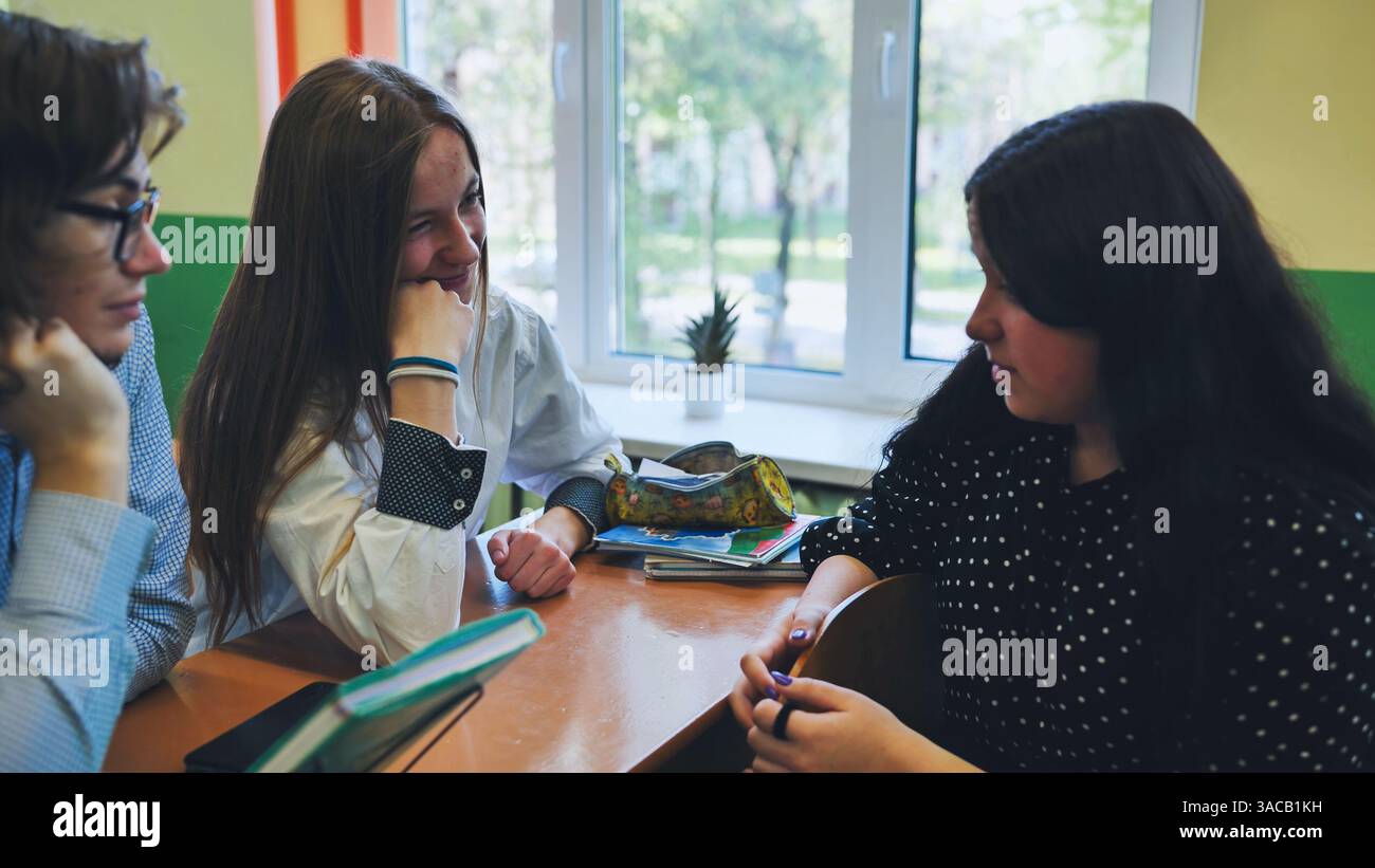 Three high school students collaborate at a desk, discussing and ...
