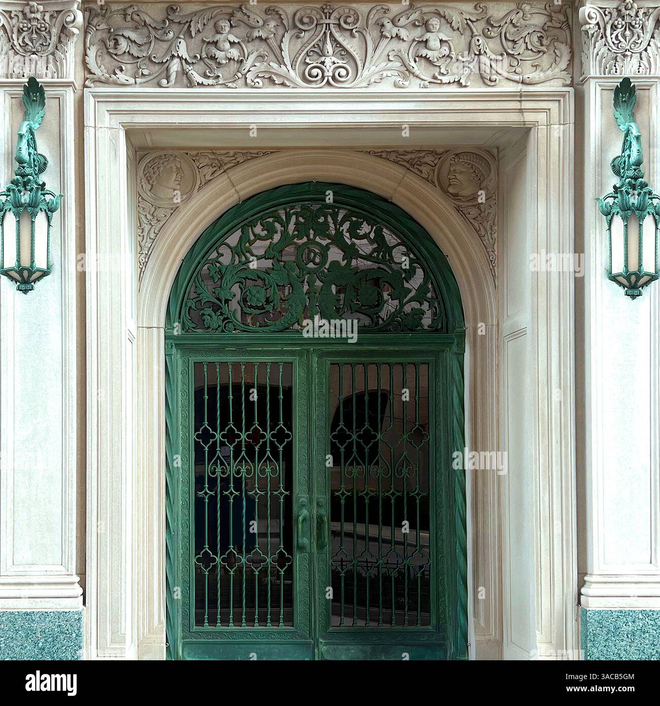 Elegant green wrought iron doors with intricate floral and animal carvings, framed by ornate architectural detailing and vintage sconces. - Smartphone Captured Stock Image