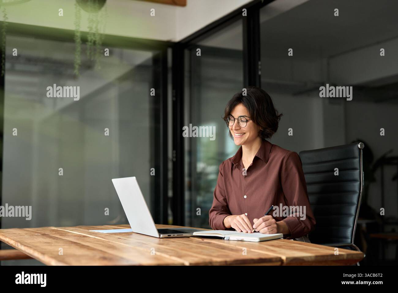 Happy busy young business woman working in office using laptop writing ...
