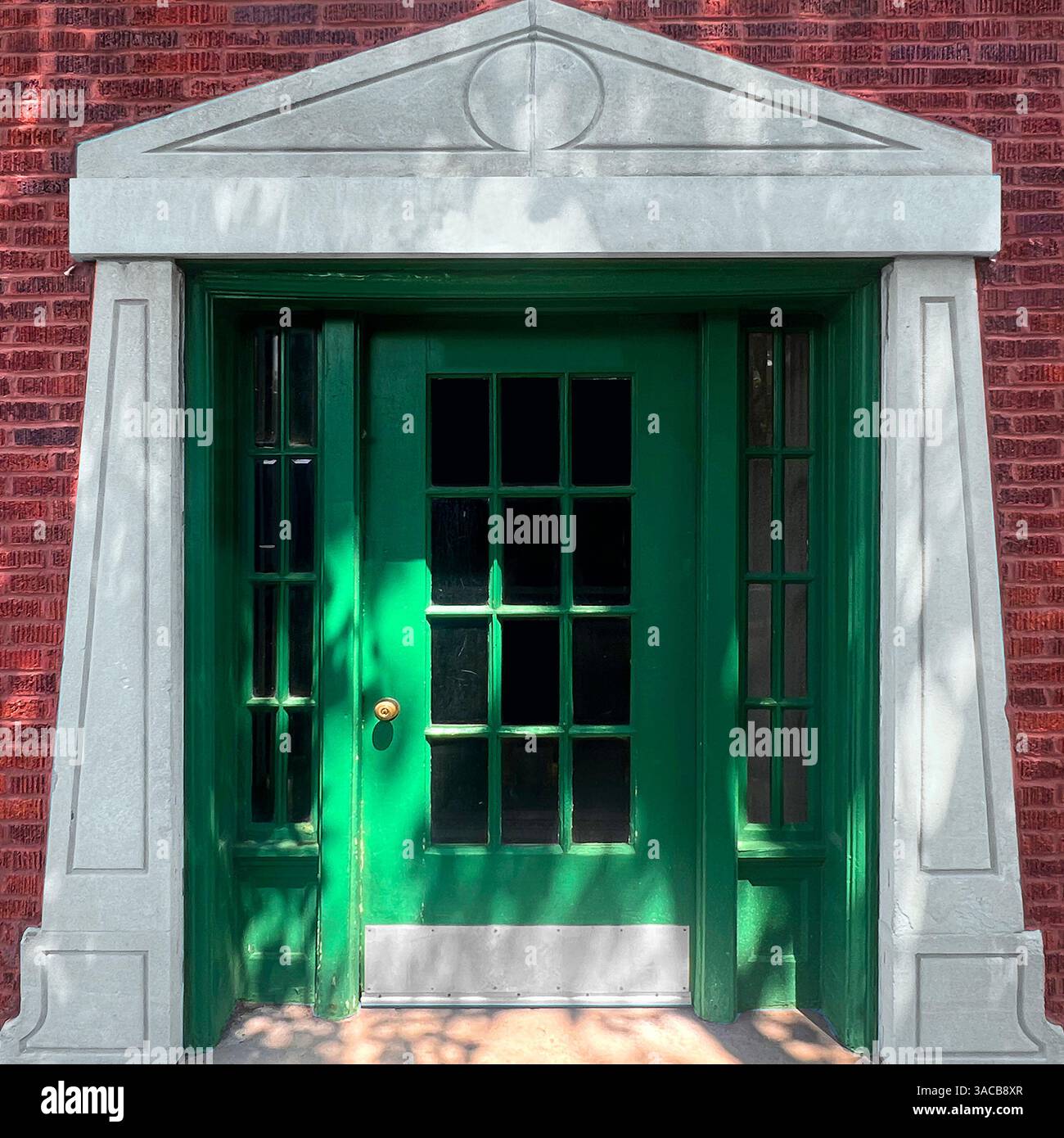 A green-door with framed by a neoclassical stone pediment and red brick facade. - Smartphone Captured Stock Image