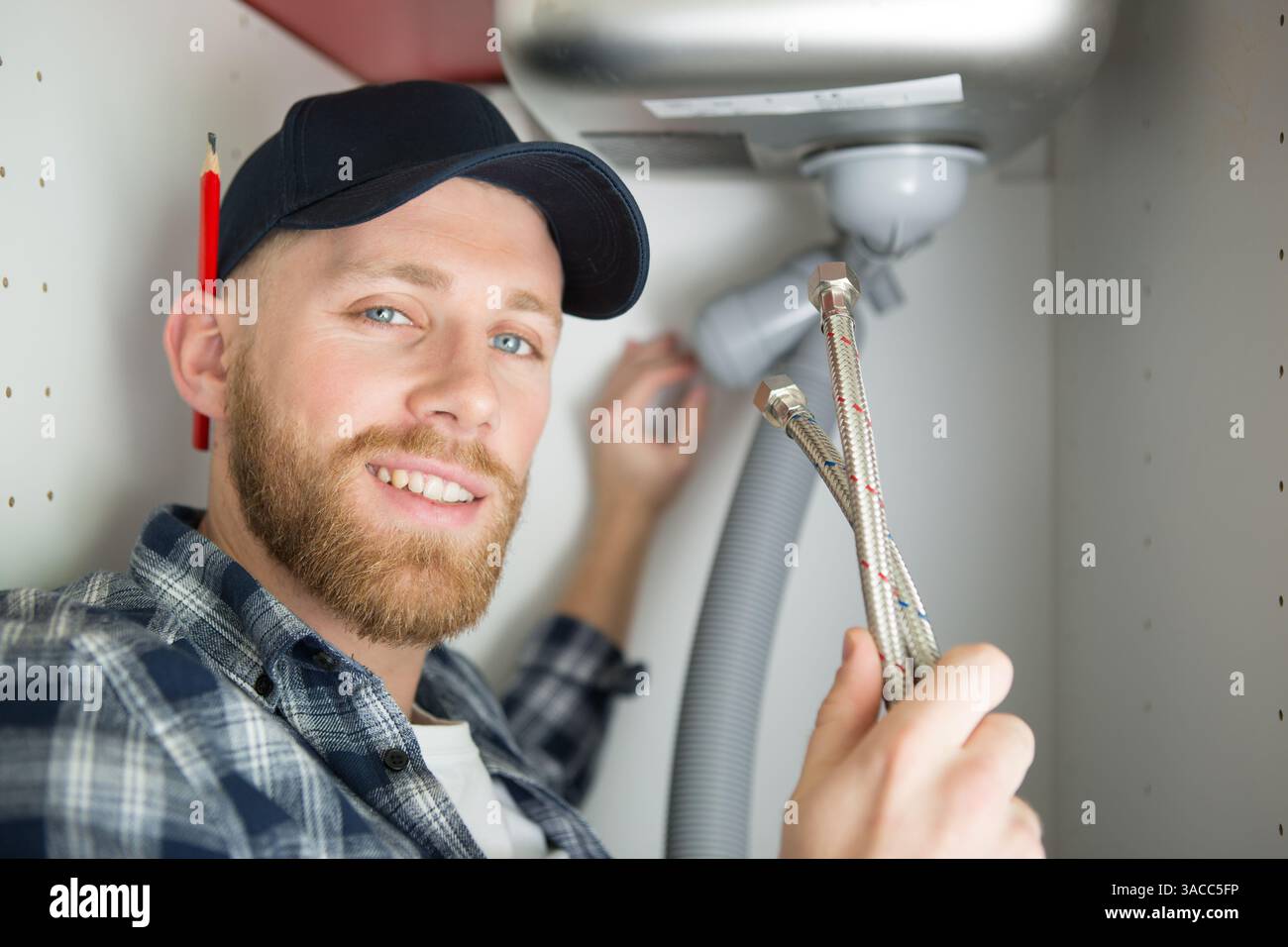 positive plumber fixing under the sink in the kitchen Stock Photo