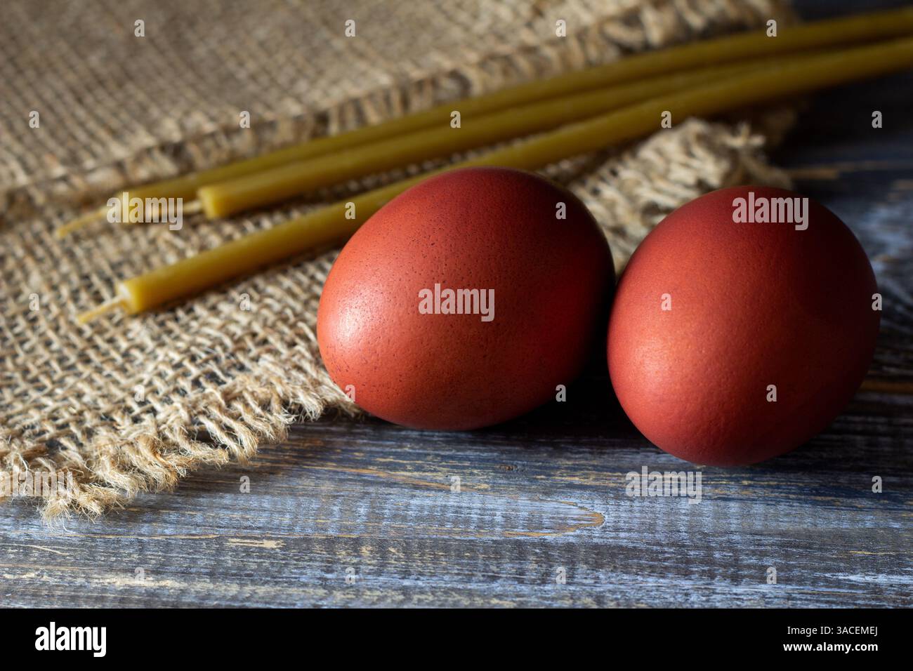 Traditional easter red dyed eggs with beeswax candles on rustic wooden and burlap background Stock Photo