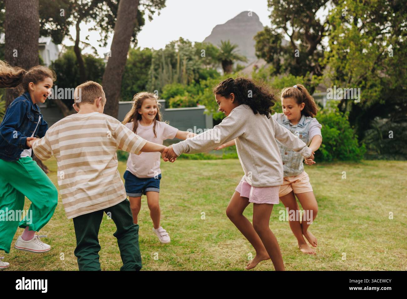 A group of children holding hands and playing in a bright, sunny park ...