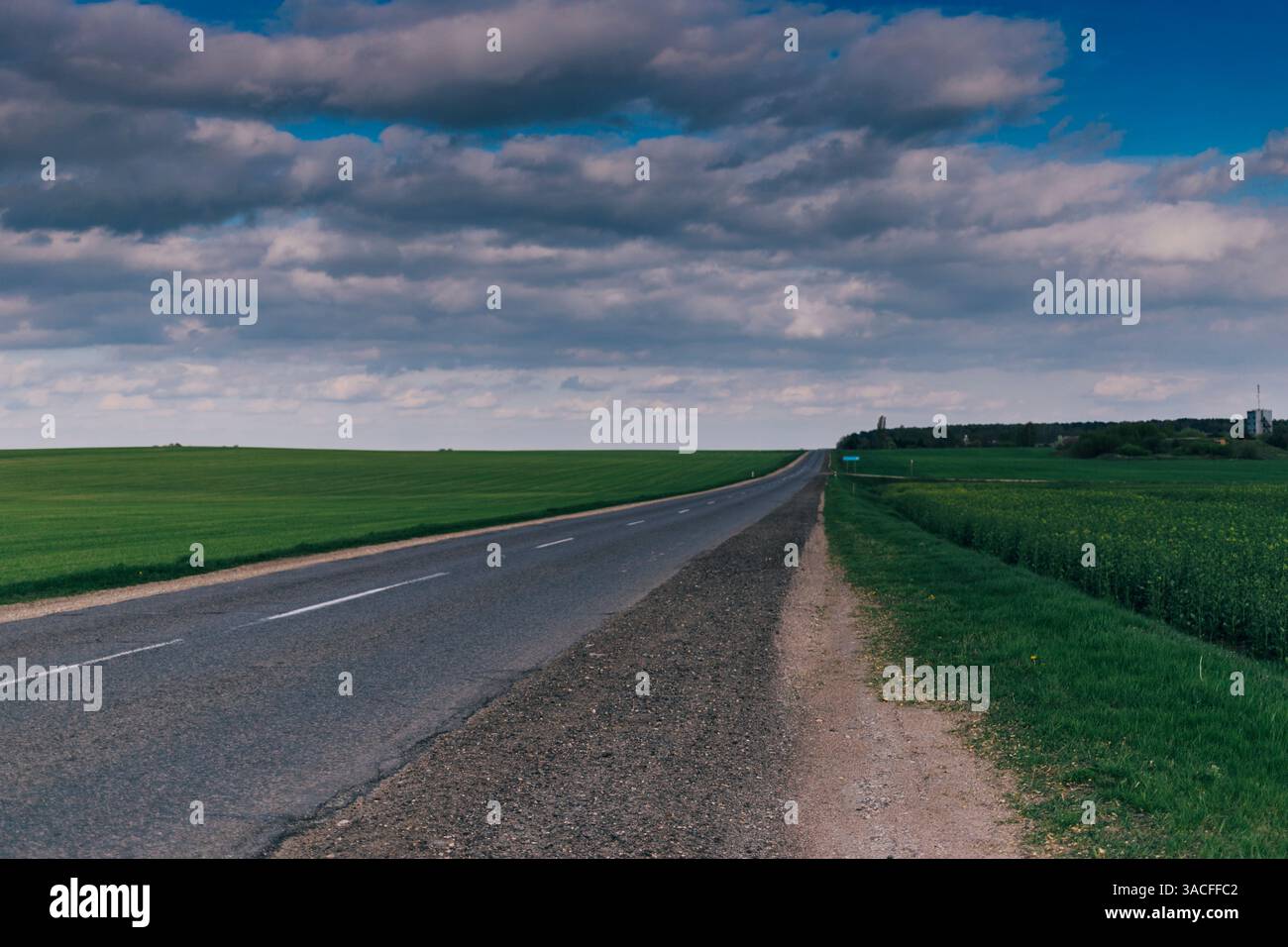 Empty Country Road Through Green Fields Under Cloudy Sky Stock Photo