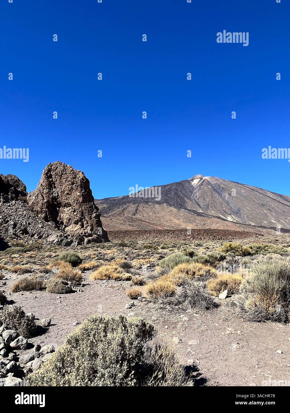 Volcanic terrain with dramatic rock formations and Mount Teide in the distance under a clear blue sky. Captured in Teide National Park, Tenerife - Smartphone Captured Stock Image