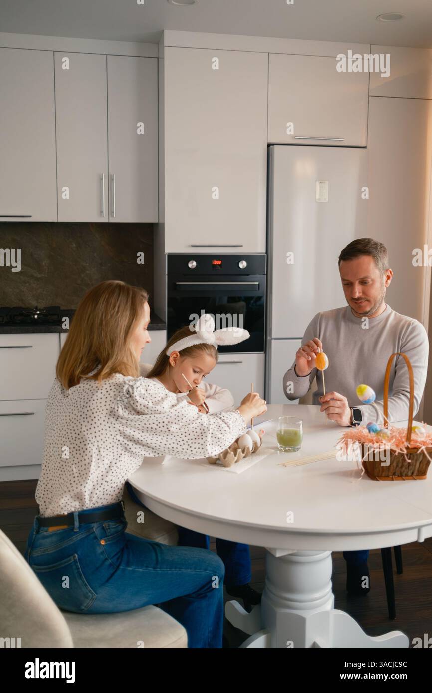 Family decorating Easter eggs together in a modern kitchen setting Stock Photo