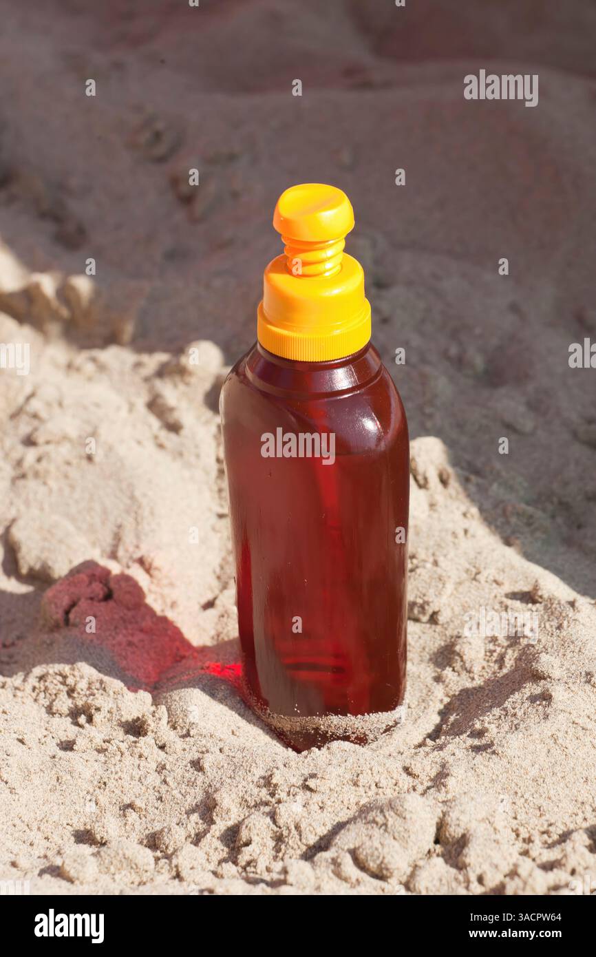 Spring Suntan Bottle of suntan lotion resting in the warm sand at the beach, soaking ...