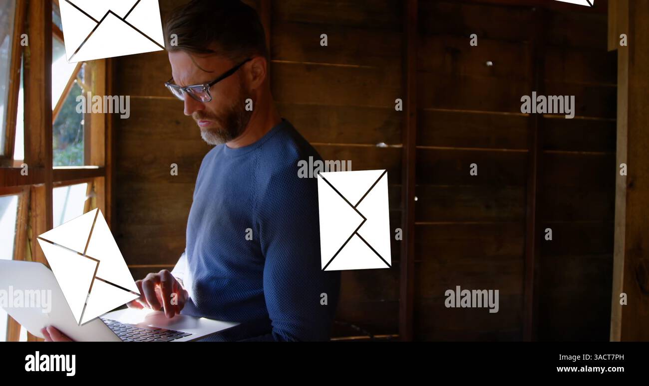 Man using laptop in rustic cabin, managing emails efficiently and focused Stock Photo