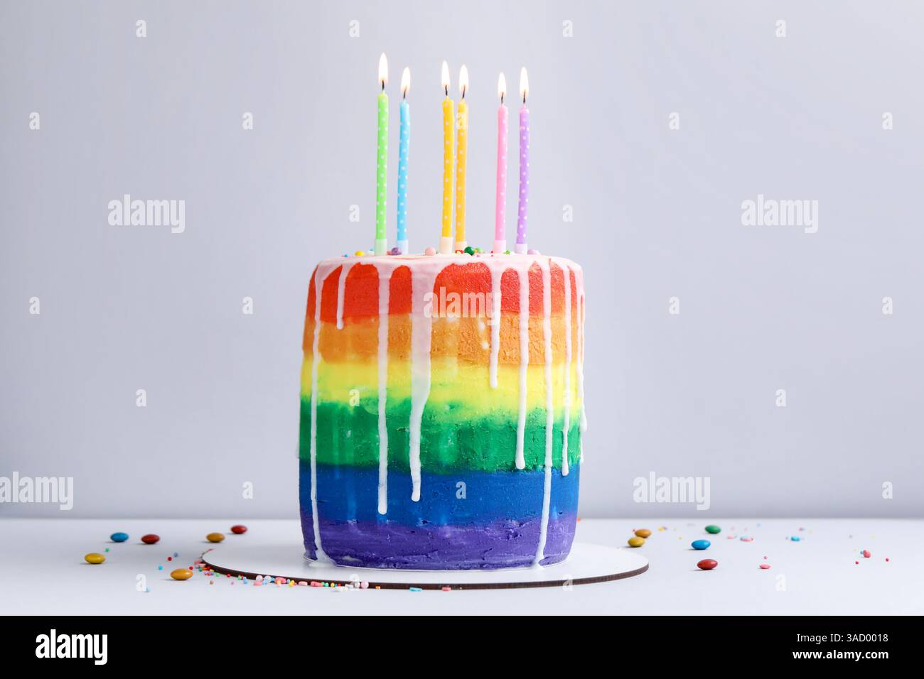 Delicious rainbow birthday cake with burning candles and sprinkles on ...