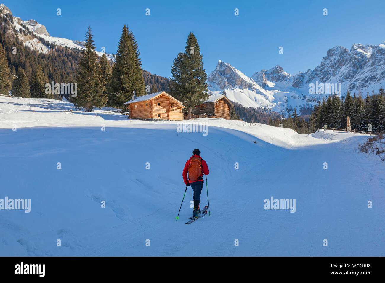 ski mountaineer in san nicolo valley near two lonely huts, winter landscape on a sunny day with snow and blue sky, pozza di fassa, autonomous province of trento, dolomites, italy Stock Photo