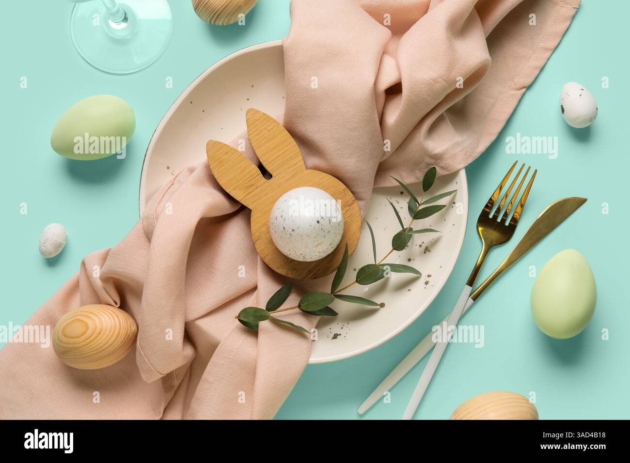 Beautiful table setting with Easter eggs and eucalyptus branch on turquoise background Stock Photo