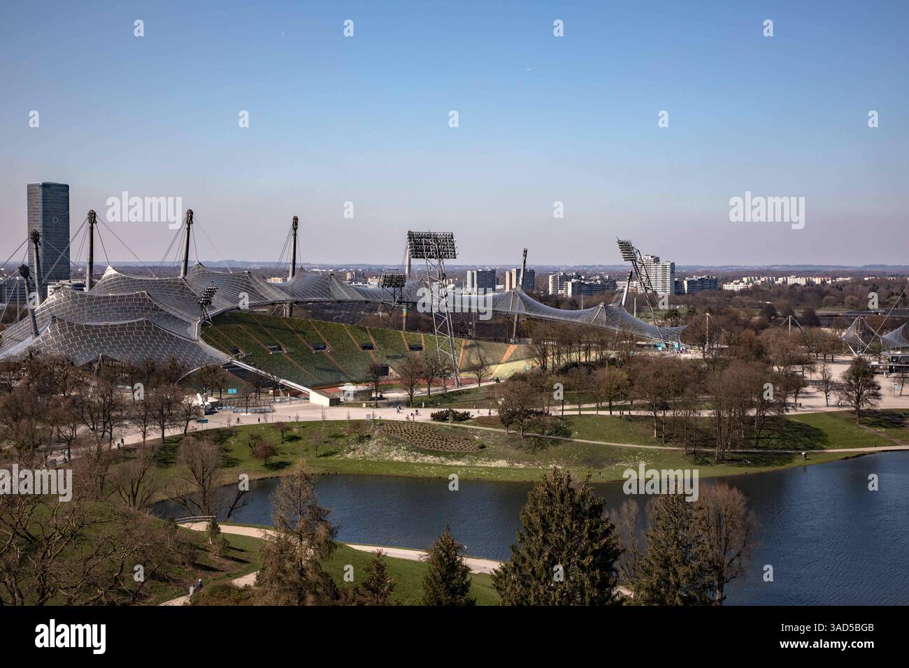 München, Deutschland 03. April 2025: Im Bild: Blick vom Olympiaberg auf den Stadtpark mit Olympiastadion und See, im Hintergrund der O2-Tower. Bayern *** Munich, Germany 03 April 2025 In the picture view from the Olympiaberg to the city park with Olympic stadium and lake, in the background the O2 Tower Bavaria Copyright: xFotostandx/xFritschx Stock Photo
