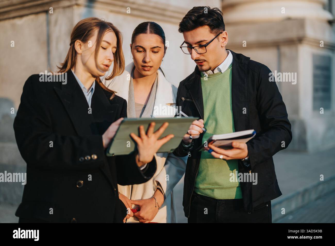 Three young professionals collaborating outdoors using a digital tablet for a project discussion. Stock Photo