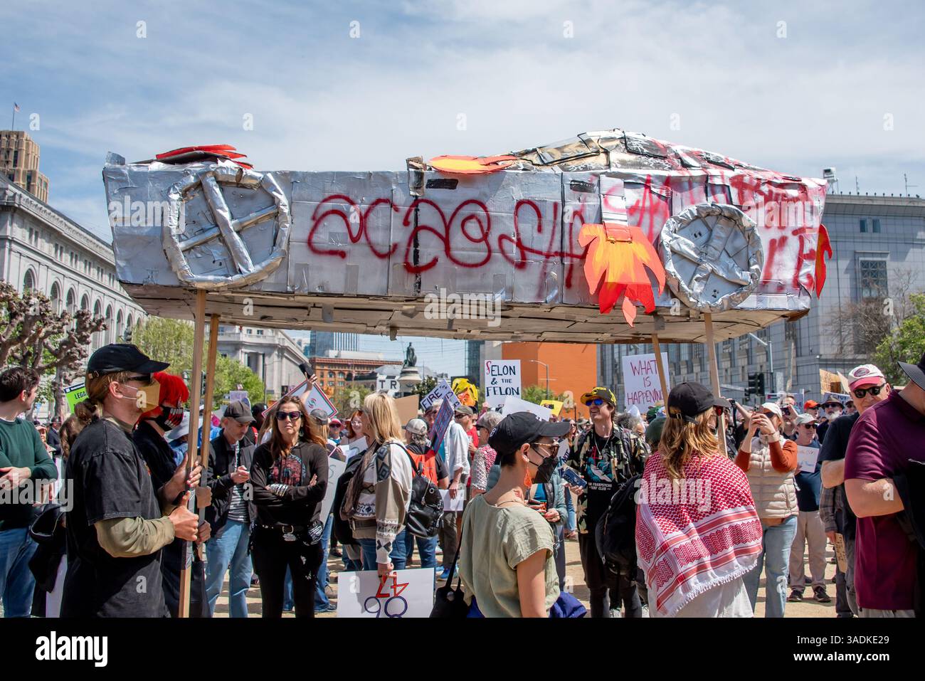 San Francisco, USA. 5th Apr 2025. Protesters at San Francisco Civic Center Plaza carry a homemade cardboard replica of a Tesla burning with spray painted graffiti and flames above their heads as the crowd thickens in the 'Hands Off!' protest against Donald Trump and Elon Musk. Credit: Shelly Rivoli/Alamy Live News - Stock Image