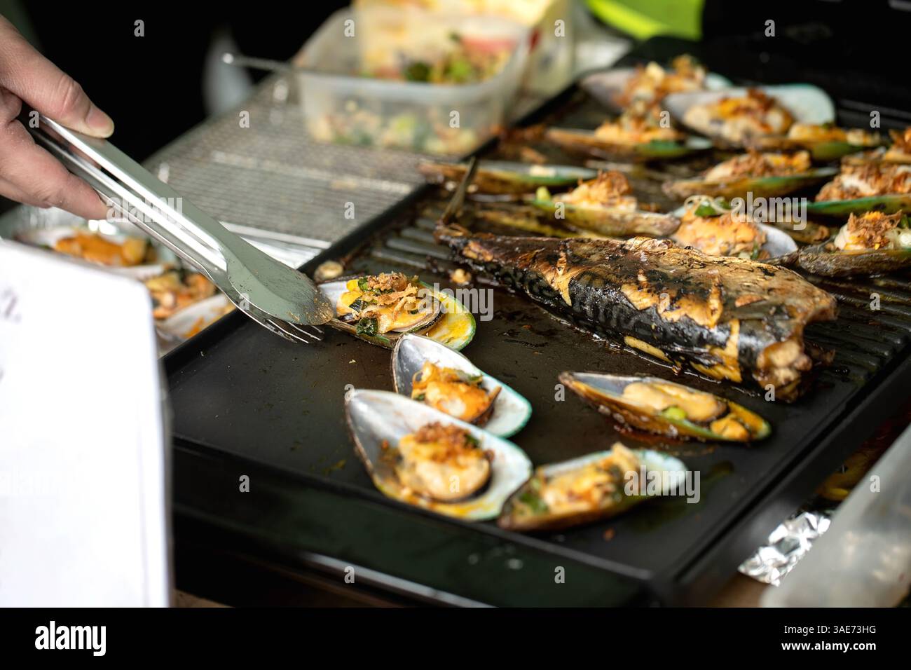 Chef grilling fresh seafood mix including mussels fish filets tongs ...